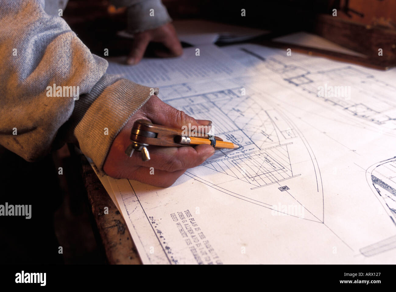 Wooden boat builder using compass or dividers on plans for a new sailing ship Stock Photo