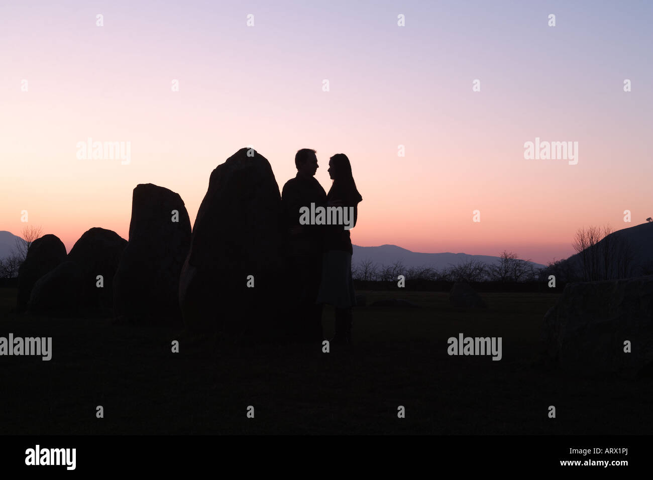 Lovers at sunset: a couple are partially silhouetted against a sunset at Castlerigg Stone Circle in Keswick, Cumbria, UK Stock Photo