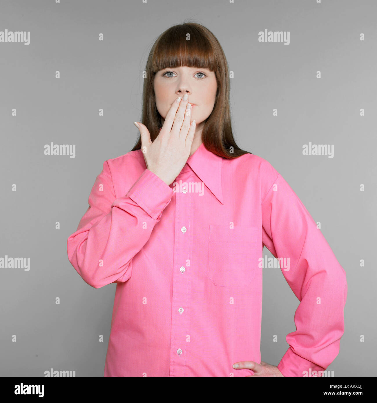 studio shot portraits of a expressive and funny red hair young woman with pink shirt putting her hand in front of her lips like oups Stock Photo