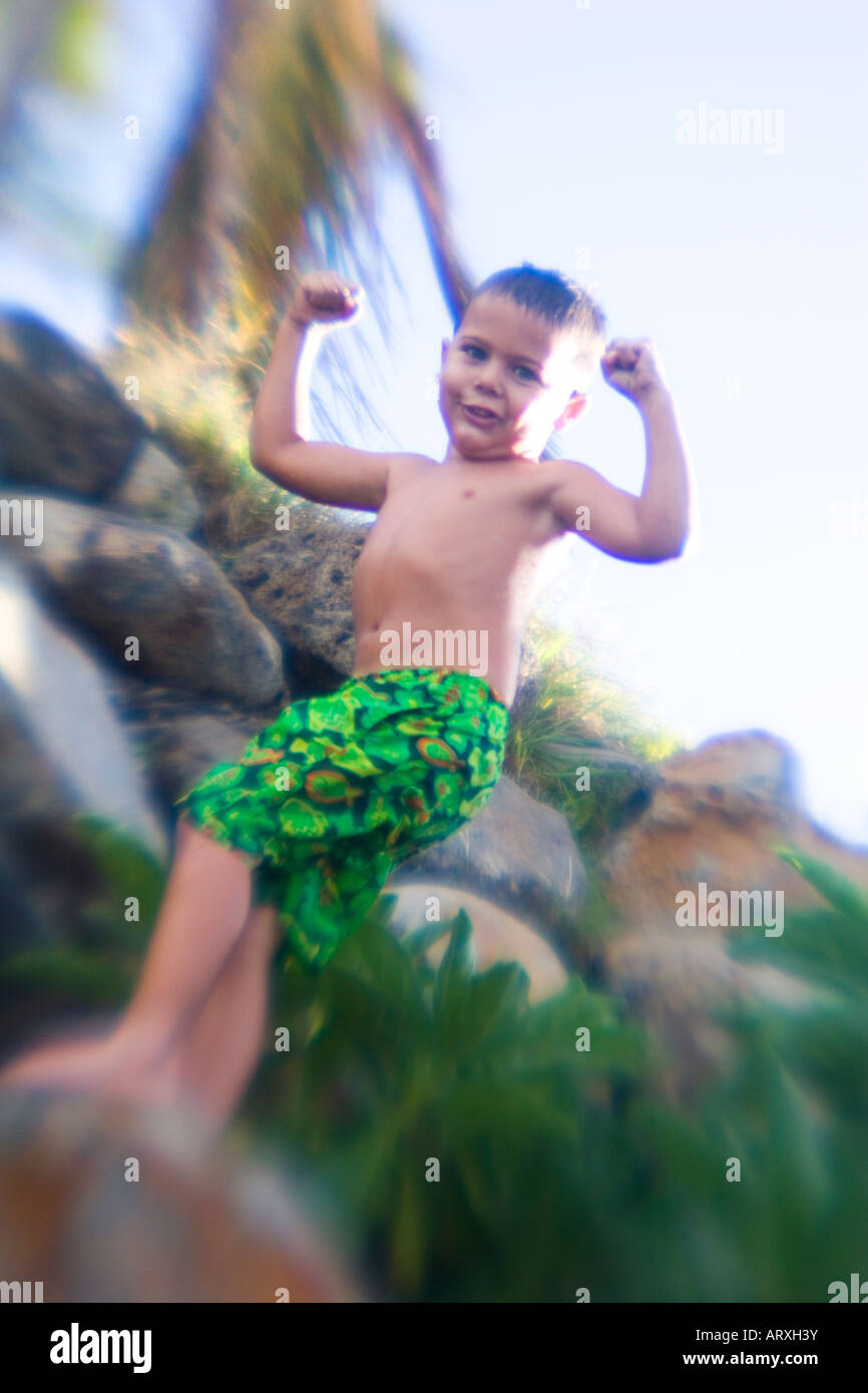 Boy in swimsuit flexes his arms. Palm tree in background. Blurred edges for artistic effect. Stock Photo