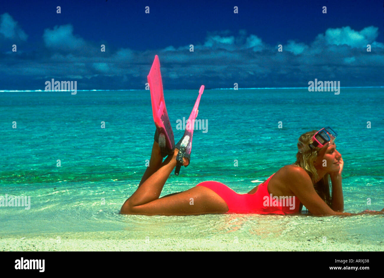 Woman wearing a pink swimsuit and snorkeling fins and mask lying in the surf on the beach Stock Photo