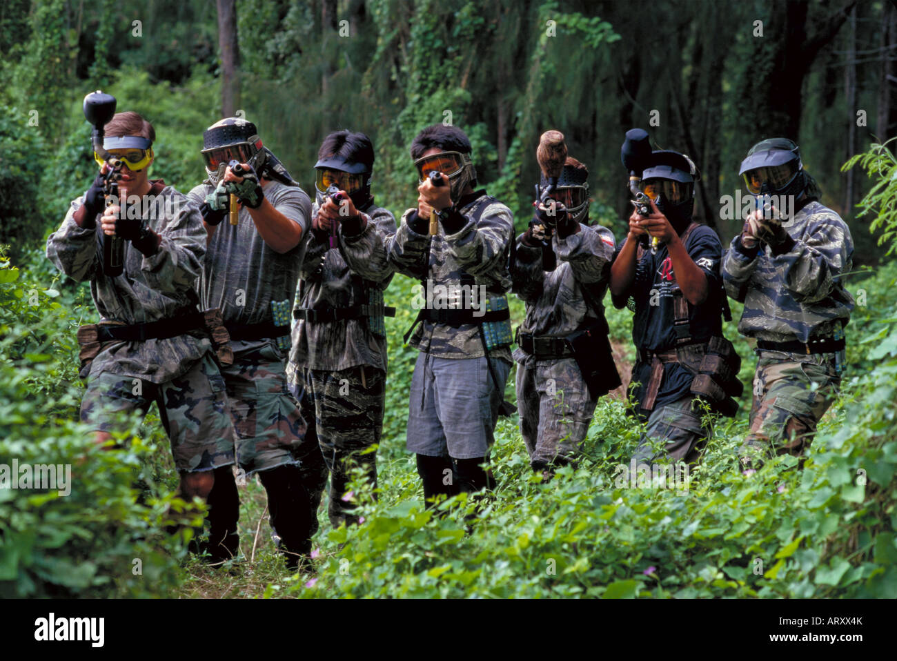 Young men with paintball guns aimed at the viewer out in the jungle
