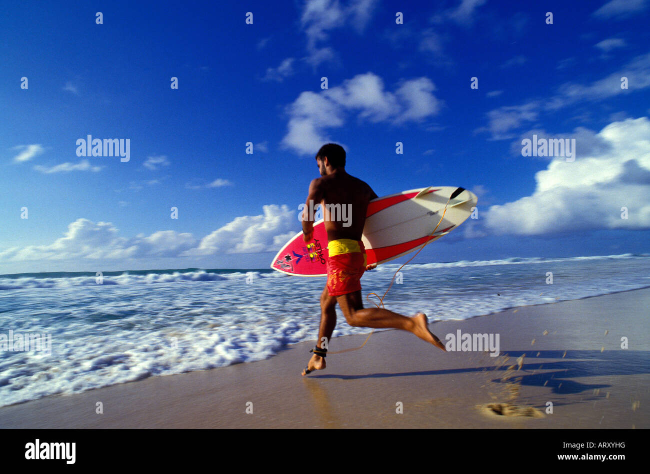 Man running out from the beach to surf with board in hand, North Shore