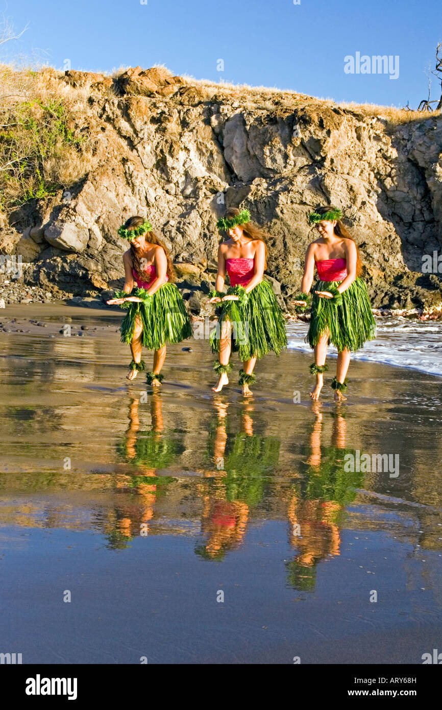 Three hula dancers in ti leaf skirts dance at the water's edge with