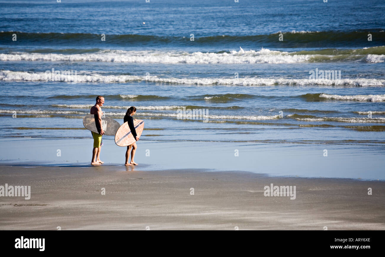 Man and woman carrying skimboards Long Beach Pacific Rim national park reserve Vancouver island Canada Stock Photo