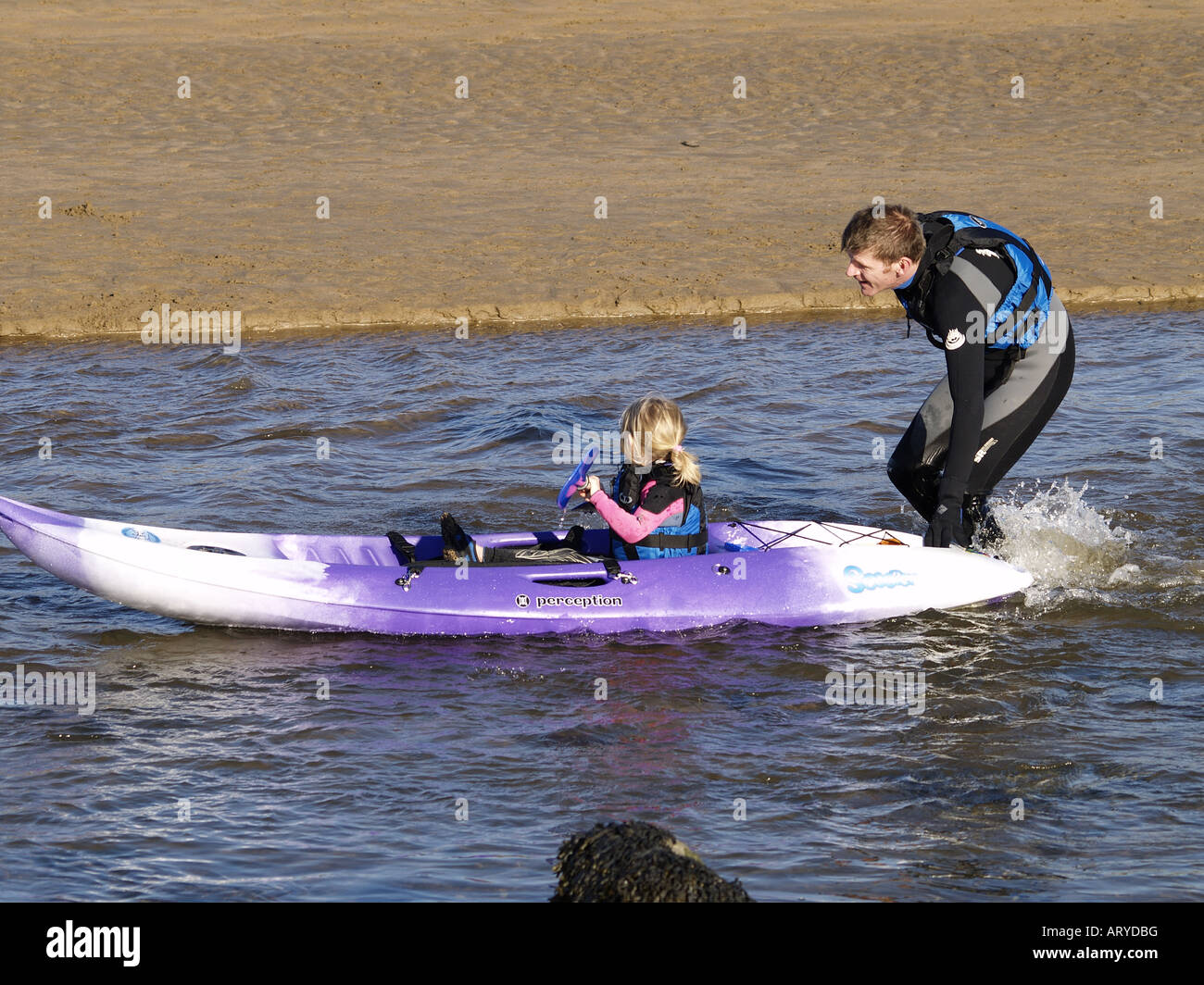 Young girl on a surf ski canoe being pushed by dad in the sea. Stock Photo