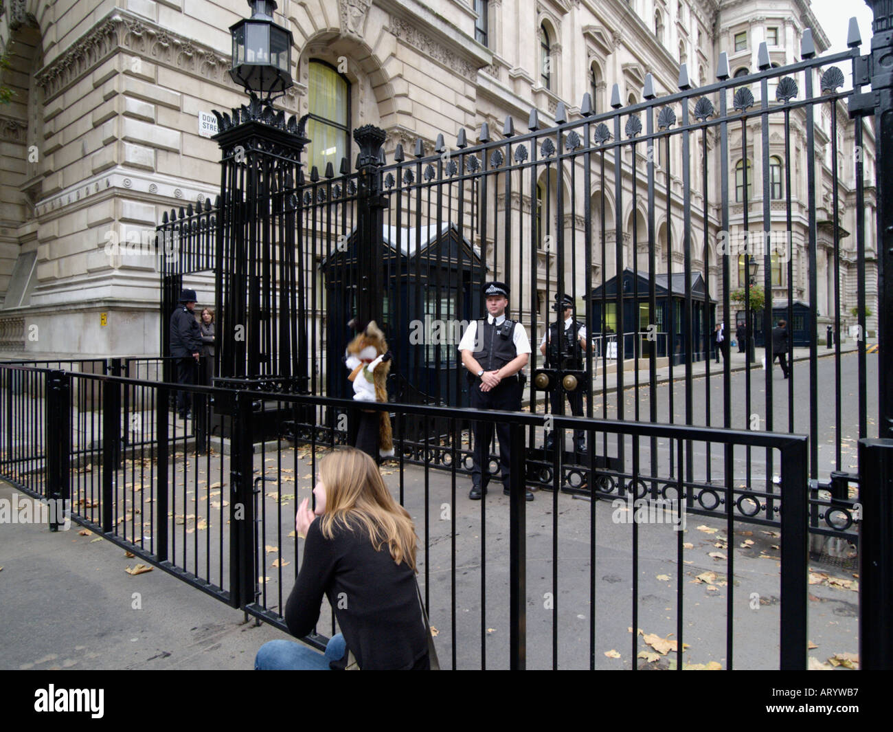 Girl playing with a hand puppet in front of the Downing Street gate that is guarded by policemen 24 7 Westminster London UK Stock Photo