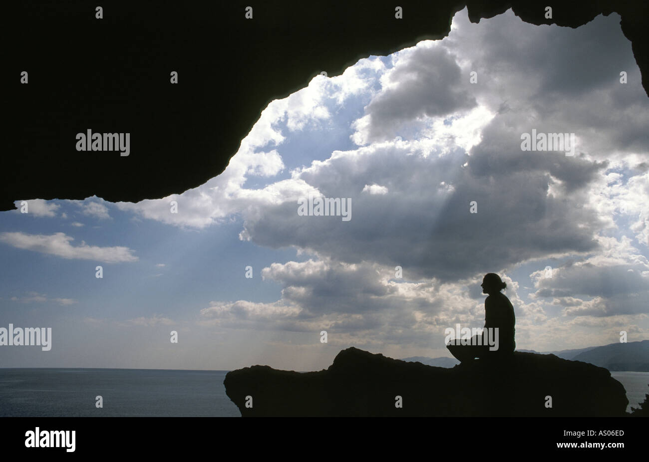 A person sits in a cave with clouds and sea Stock Photo