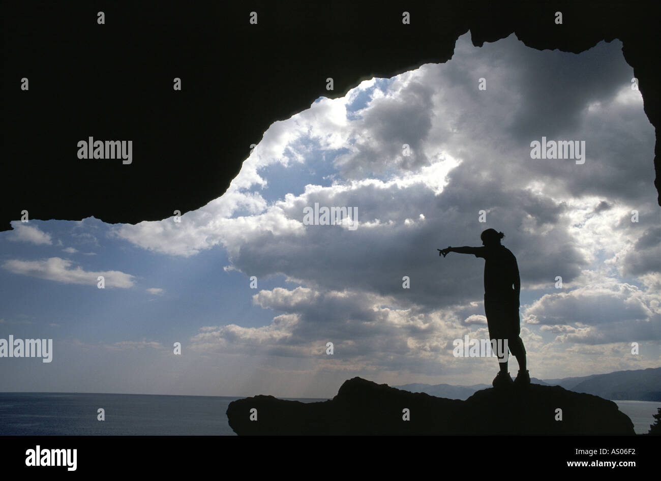 A person stands in a cave with clouds and sea Stock Photo