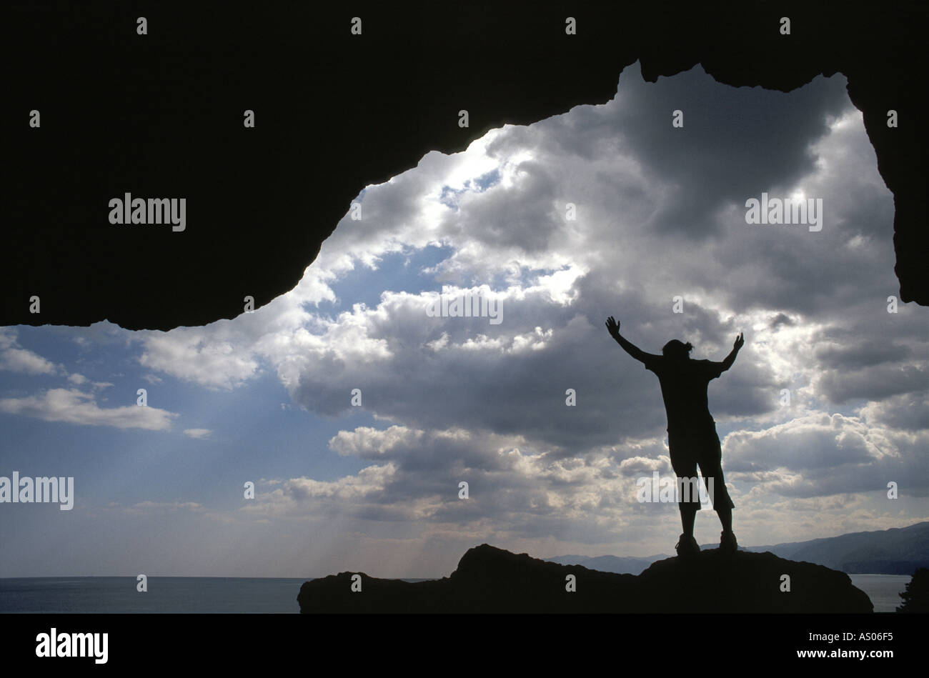 A person stands in a cave with clouds and sea Stock Photo
