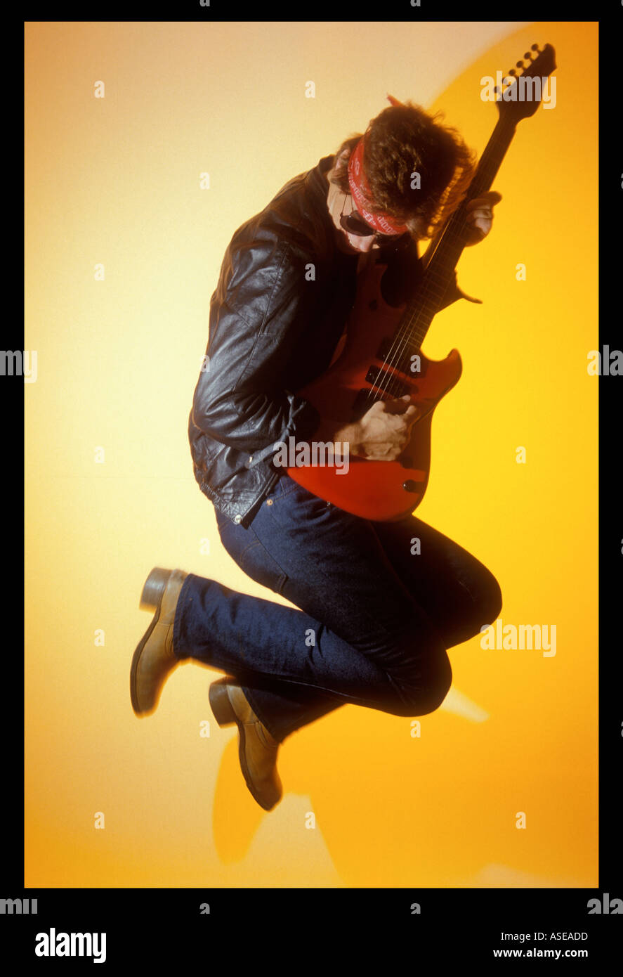 rock and roll musician leaps into the air and belts out a riff on an electric guitar Stock Photo