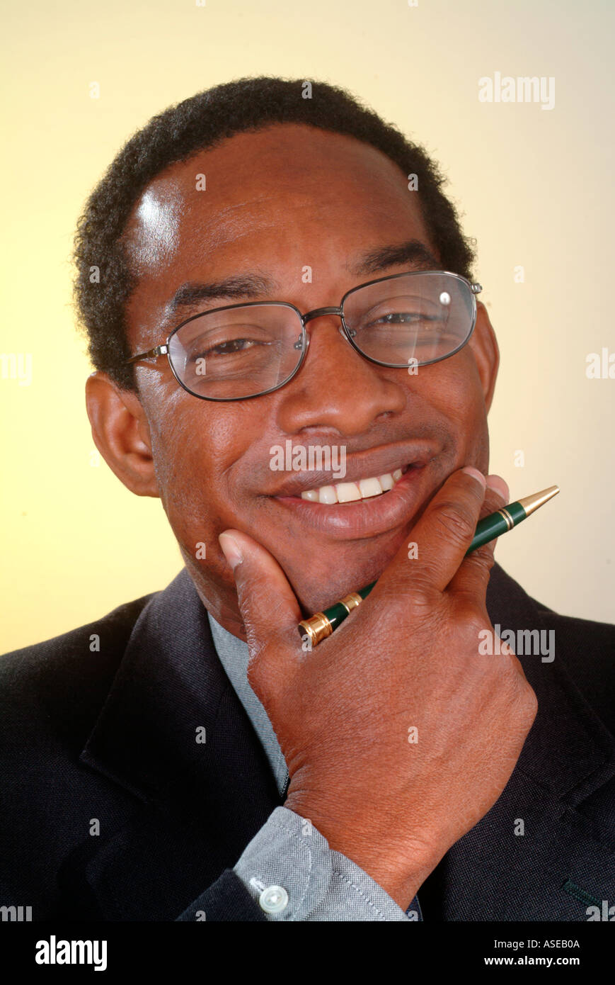 A black businessman with a pen in his hand in suit tie and glasses smiles during a portrait Stock Photo