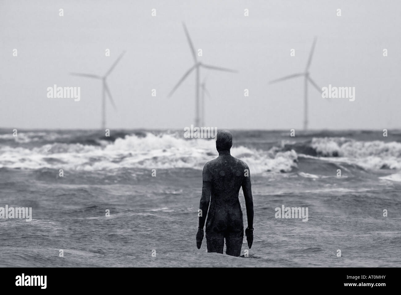 Antony Gormley sculpture of man looking out to sea towards wind power turbines Crosby Beach Merseyside England UK GB Stock Photo