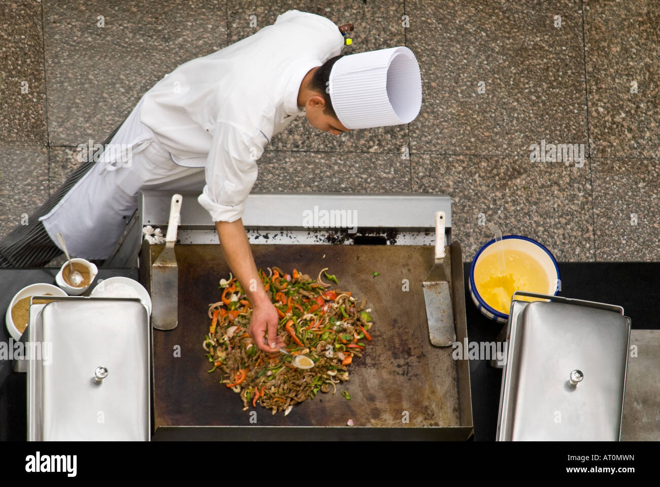 Horizontal aerial close up of a chef in whites adding ingredients to a freshly prepared stir fry outside on a hotplate Stock Photo