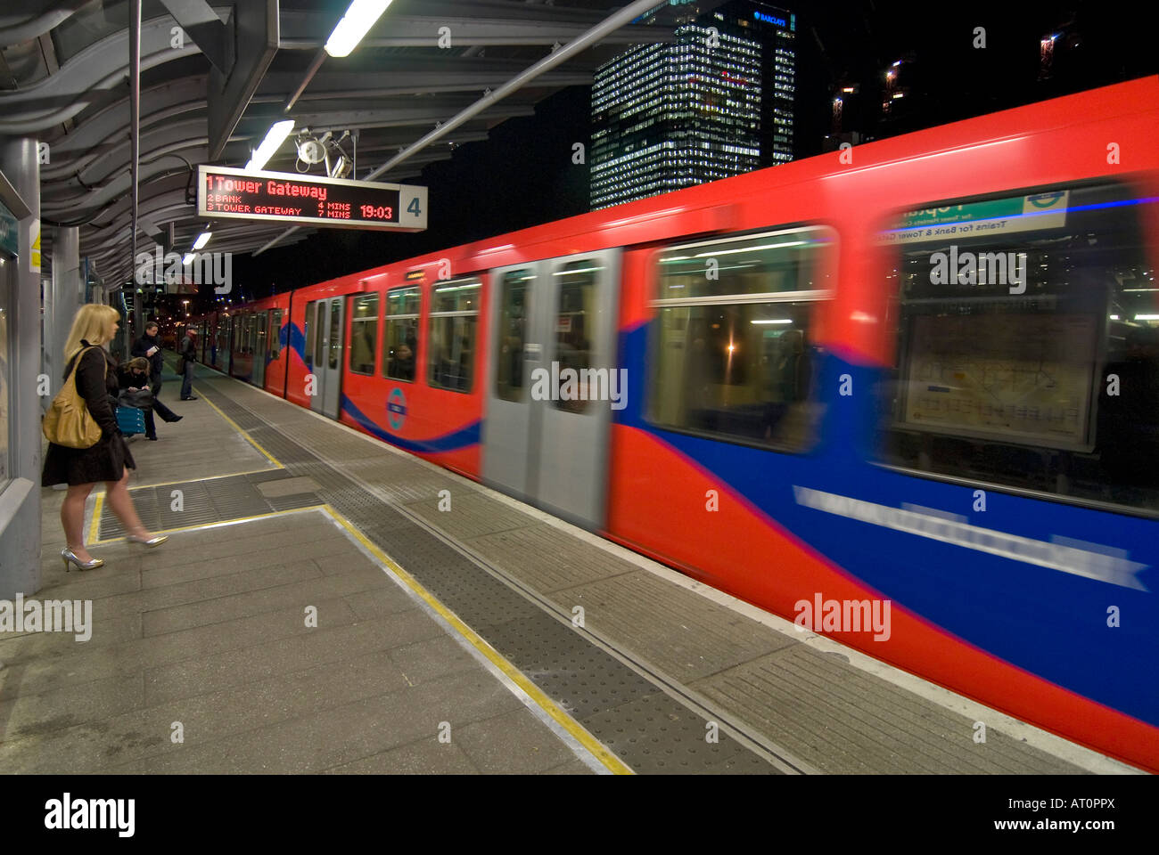 Horizontal wide angle of a Docklands Light Railway train arriving at Poplar station with people waiting on the platform at night Stock Photo