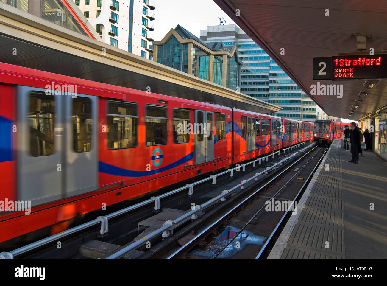 Horizontal wide angle of two Docklands Light Railway trains pulling into and out of South Quay station with passengers waiting. Stock Photo