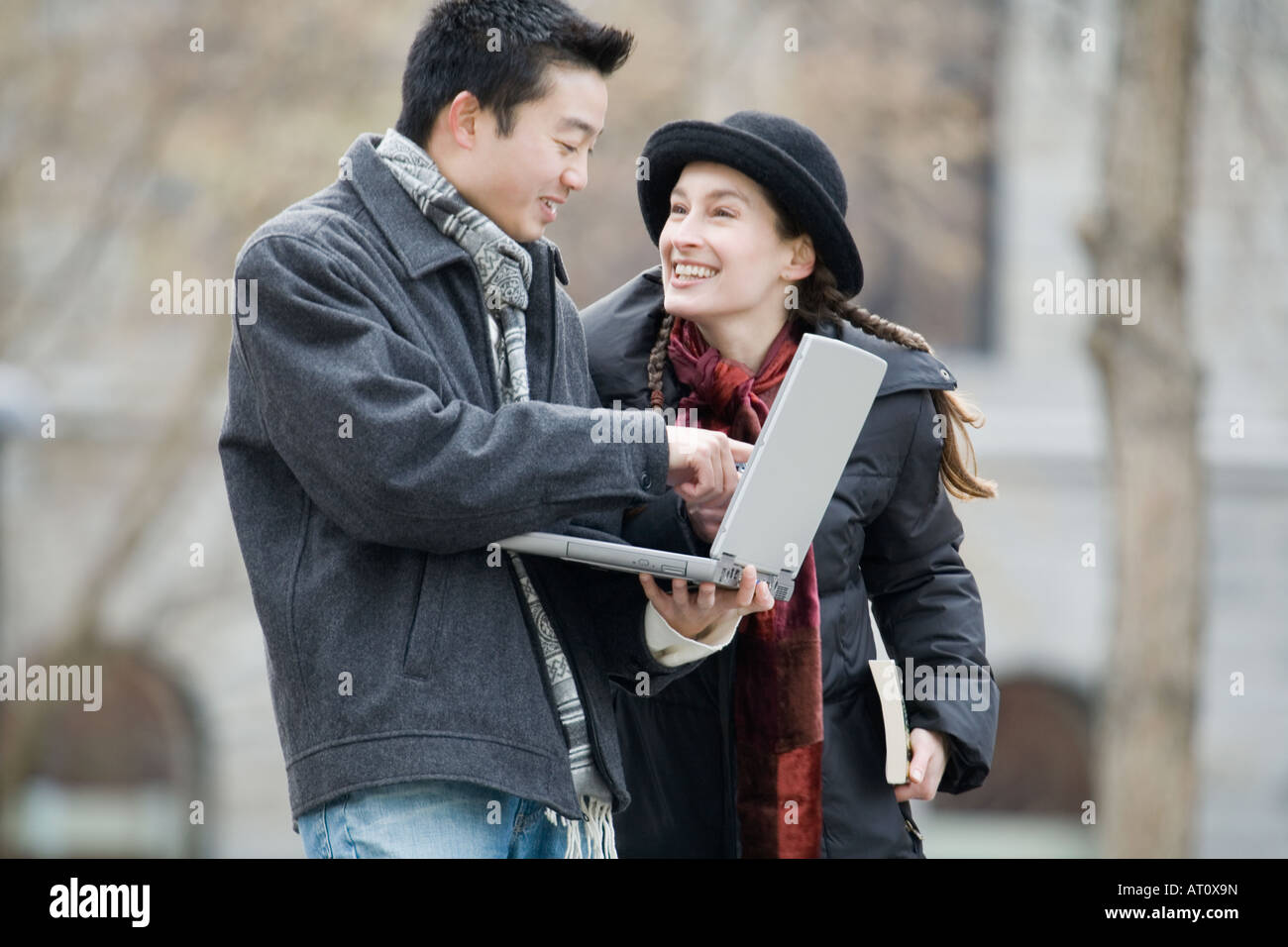 Side profile of a young man using a laptop and a young woman looking at her Stock Photo