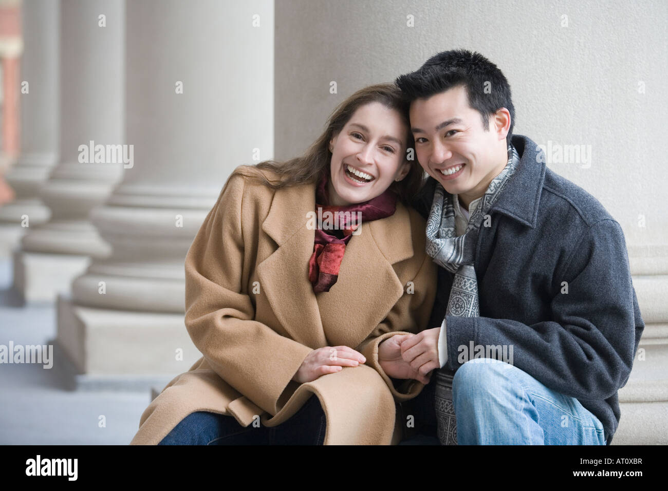 Portrait of a young couple sitting in front of a column and smiling ...