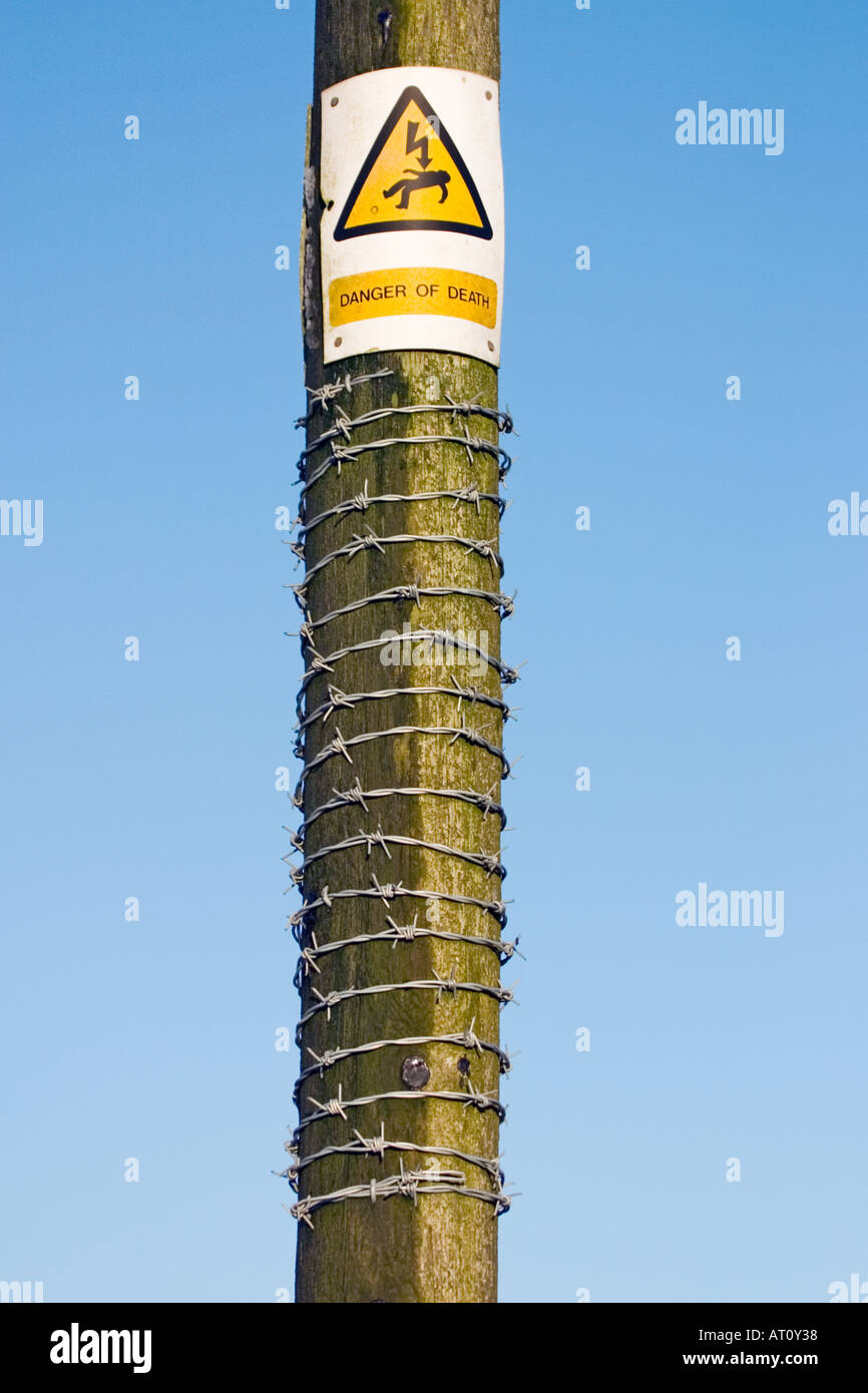 Electricity pole with barbed wire and warning sign Stock Photo