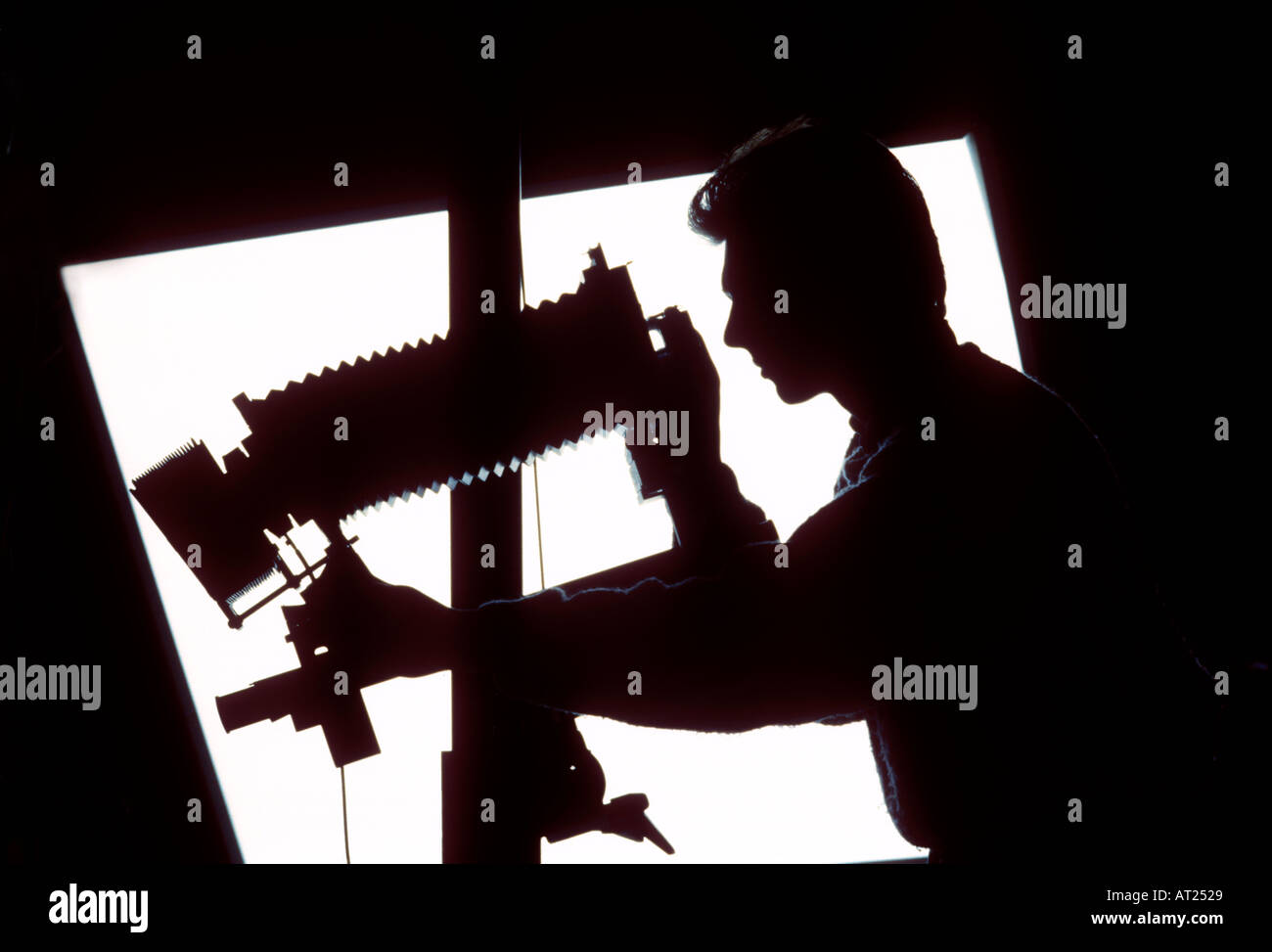 Film Camera Studio still life photographer with 5x4 film camera on tripod stand with lens image plane movement applied, silhouetted against pool light Stock Photo