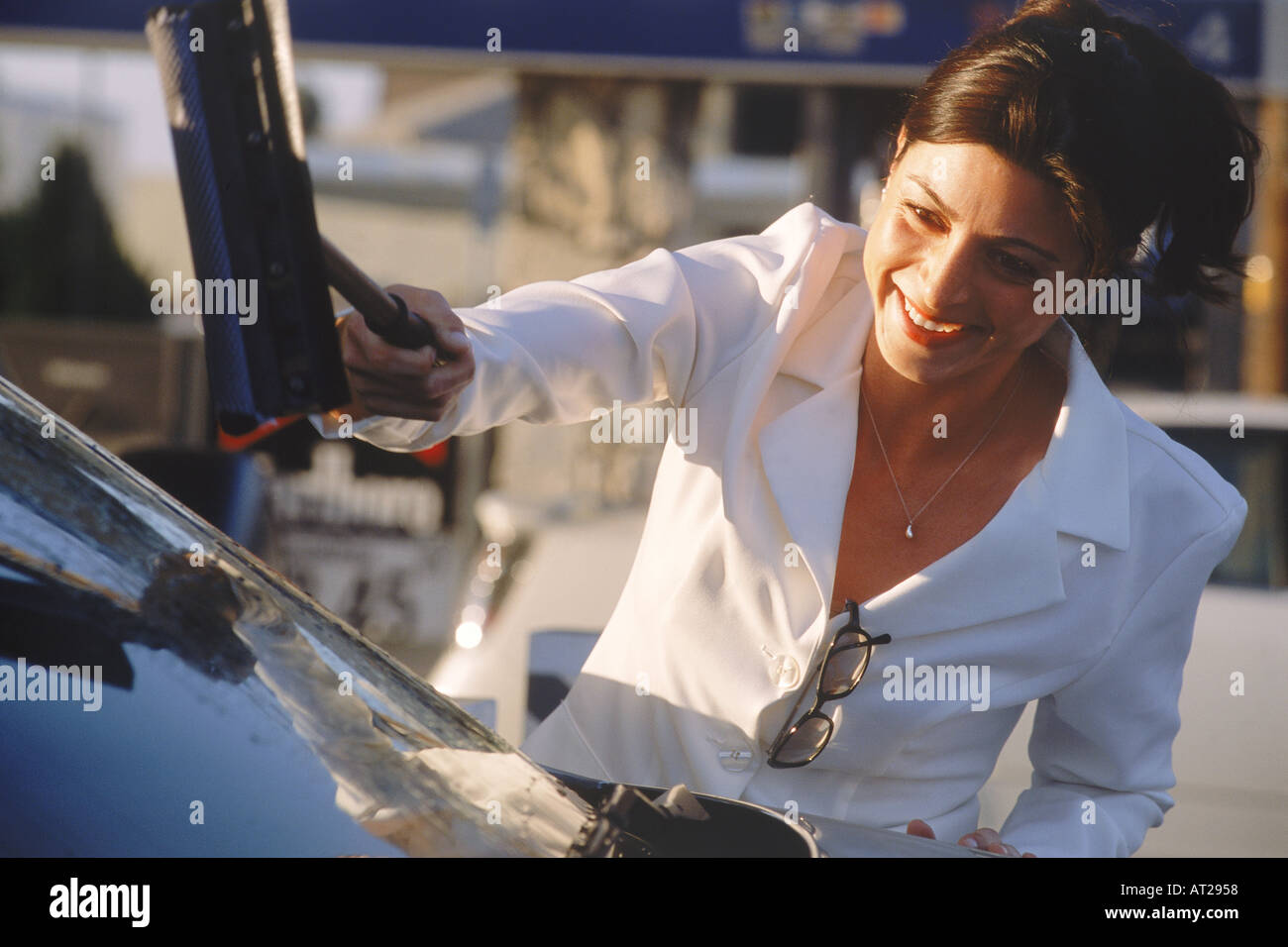 Woman in business suit cleaning windshield with handle wipe at self service gas station in USA Stock Photo
