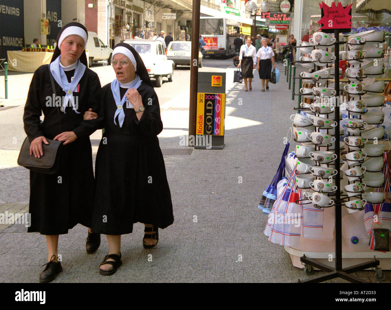 Nuns walking down a street filled with religious souvenir shops in the town of Lourdes in south west France Stock Photo