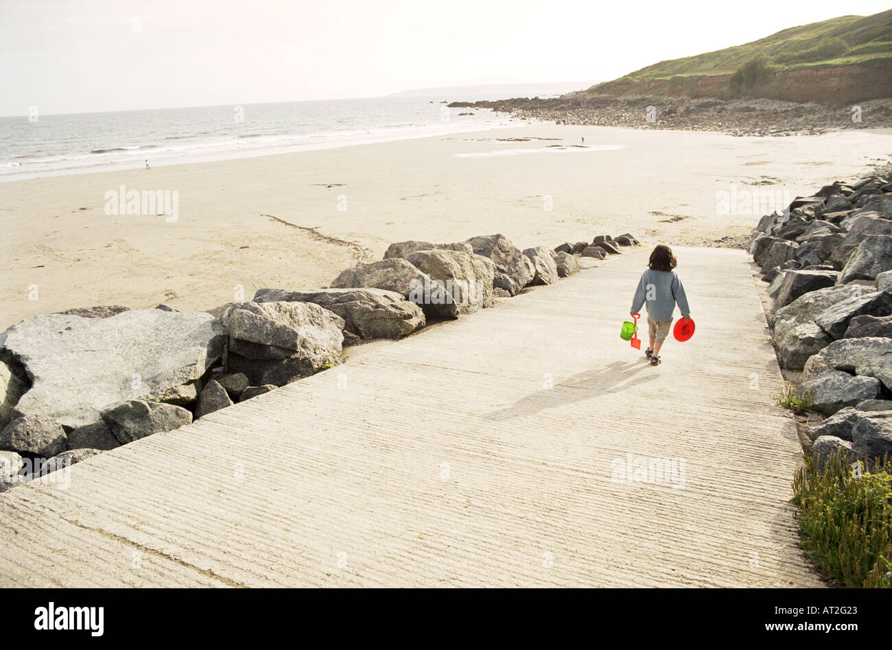 A small girl walking to the beach carrying a bucket and spade Stock Photo