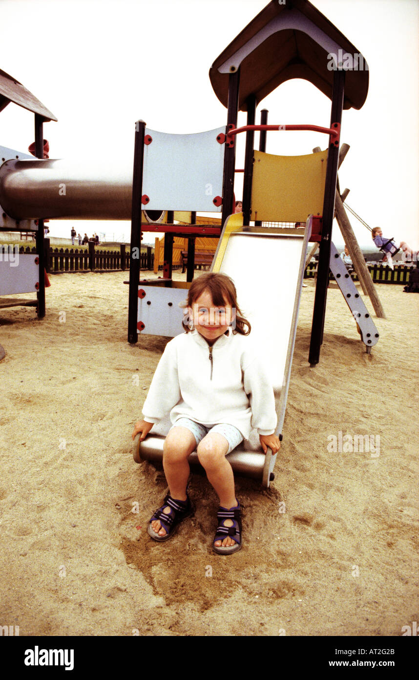 A girl sitting at the bottom of a slide in a playground Stock Photo
