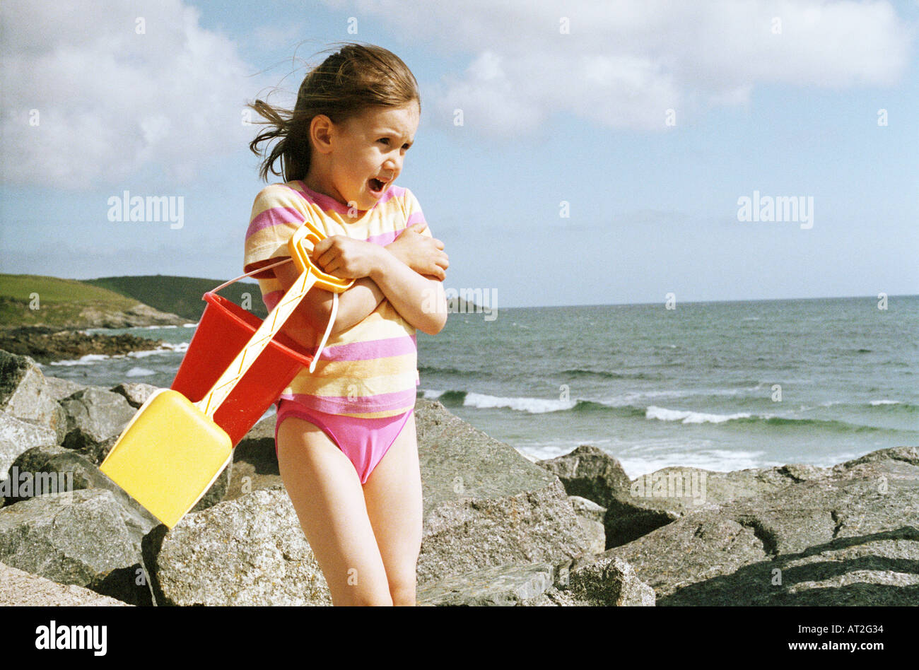 A small girl standing next to the sea holding a bucket and spade Stock Photo
