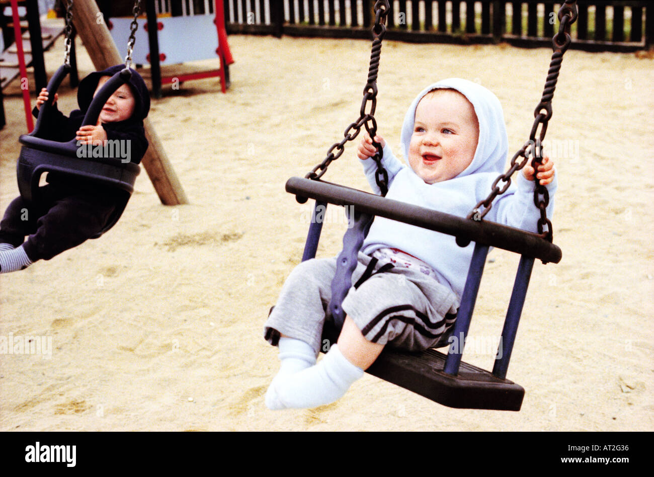 Two babies sitting on swings in a playground Stock Photo