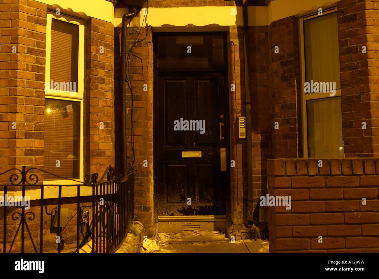 black wooden door entrance to red brick run down building with security intercom buzzer and litter Stock Photo