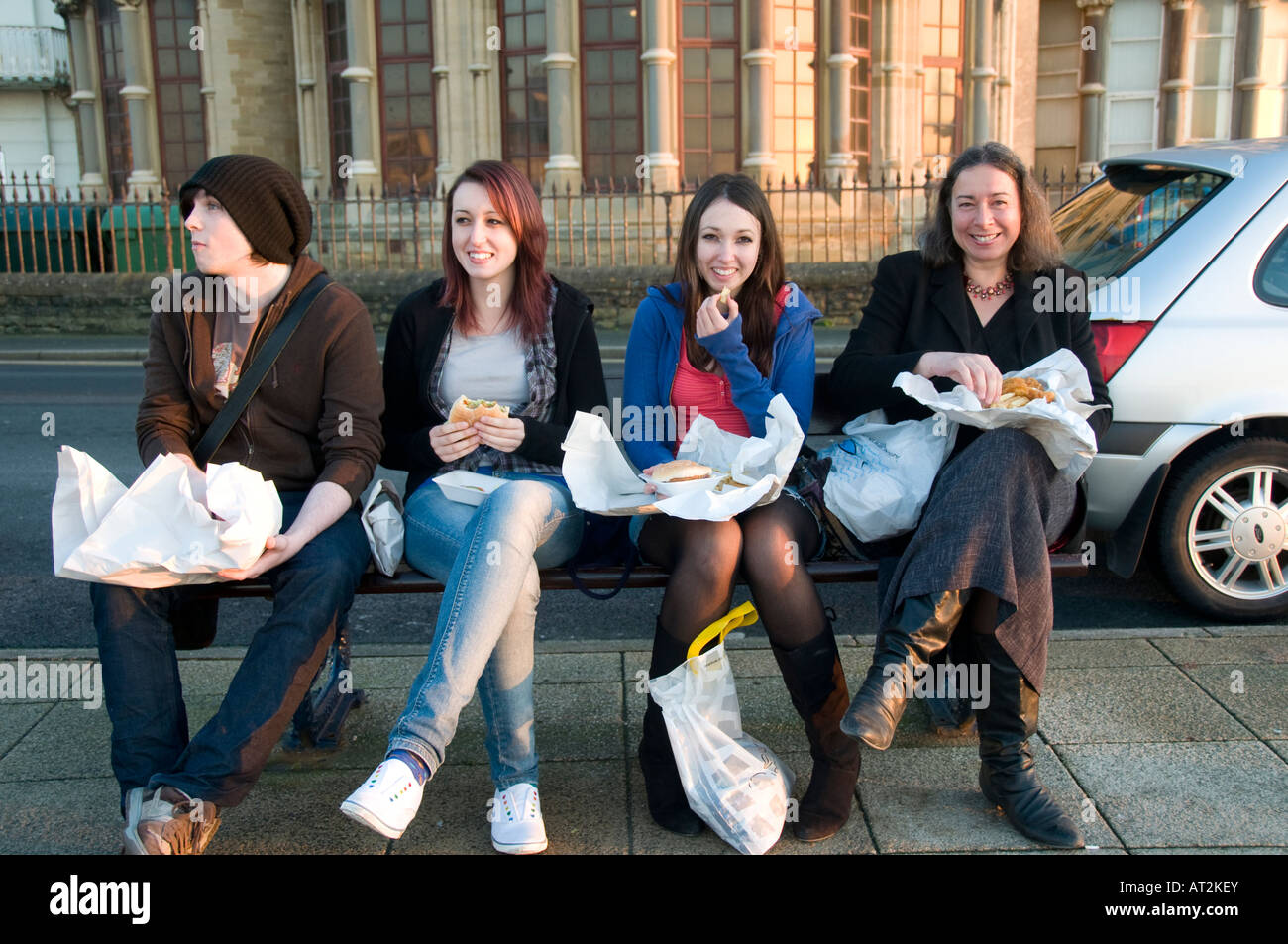Mother and three teenage children eating fish and chips on a bench Aberystwyth promenade, evening Stock Photo