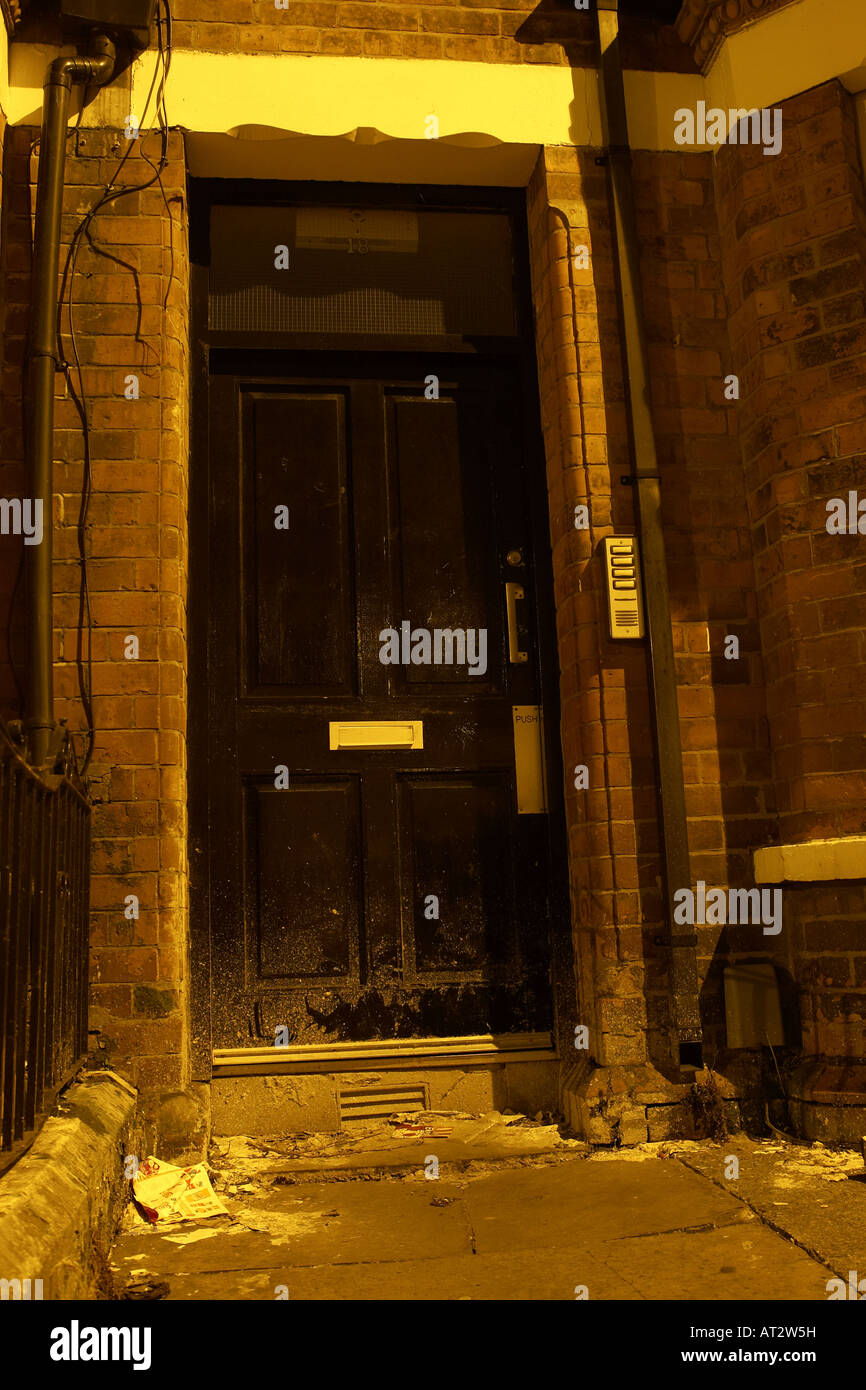 black wooden door entrance to red brick run down building with security intercom buzzer and litter Stock Photo