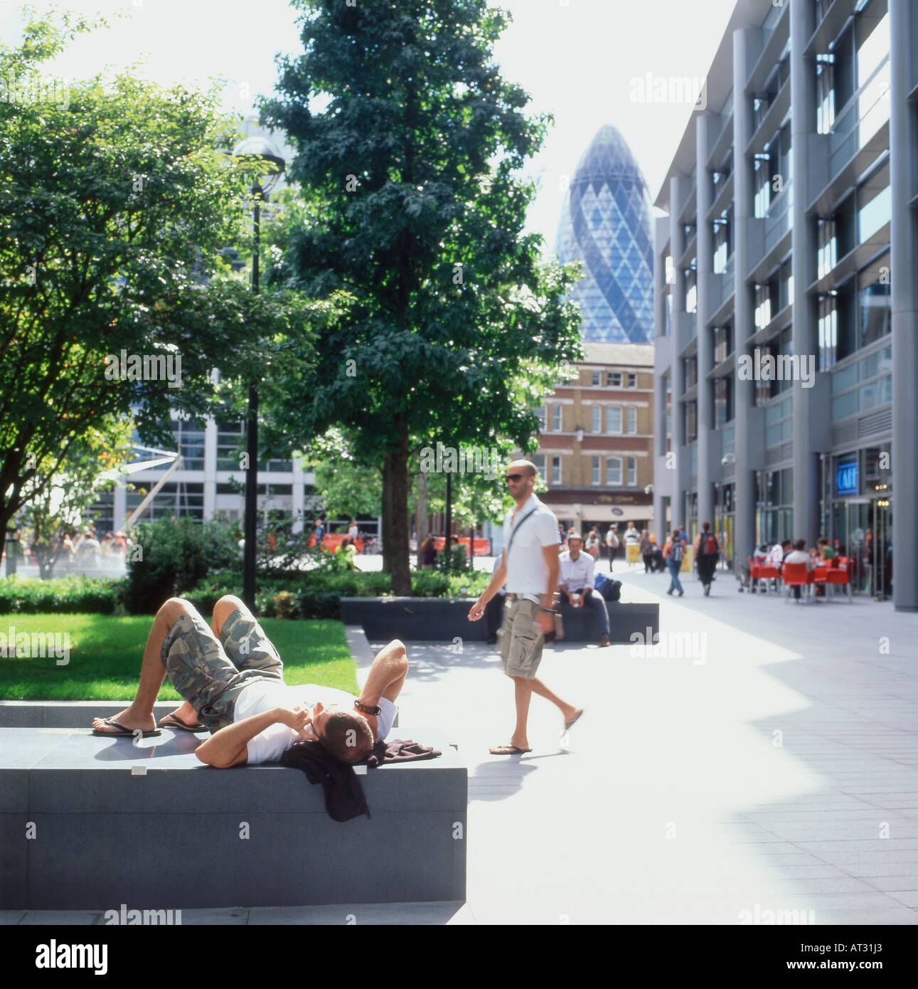 A view of the gerkin gherkin building from Bishops Square and a man lying down talking on his mobile phone in Spitalfields City of London England UK Stock Photo
