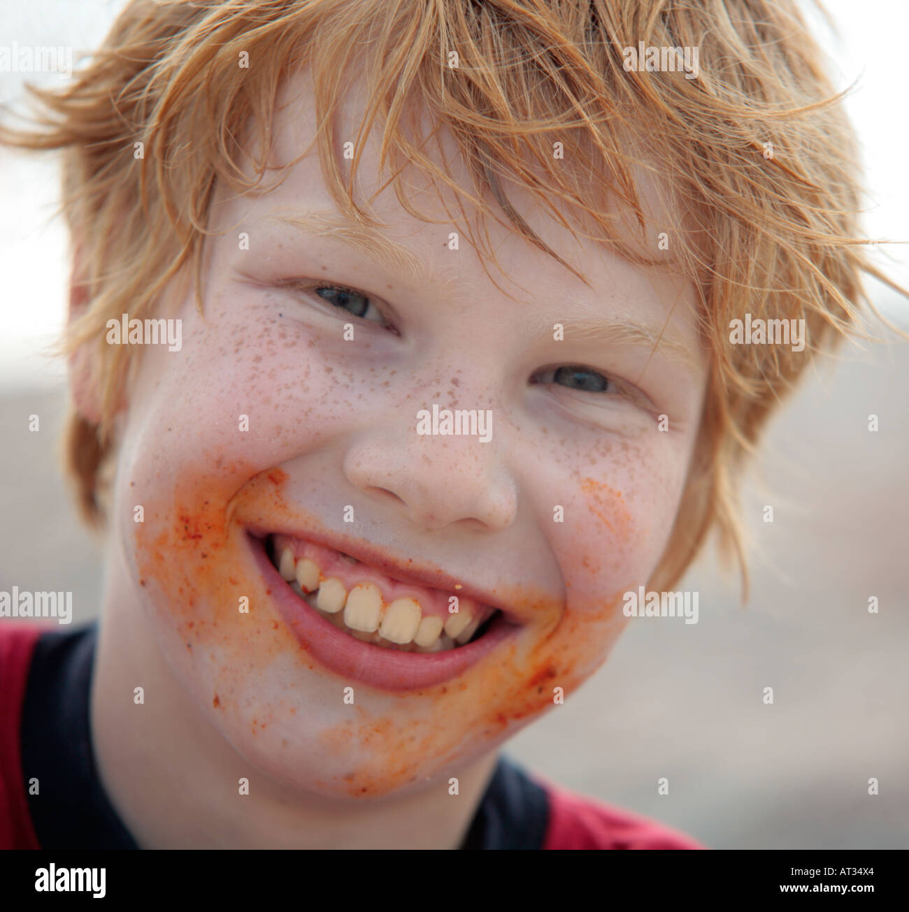a young red haired boy with freckles and a very dirty face smiling into the camera Stock Photo