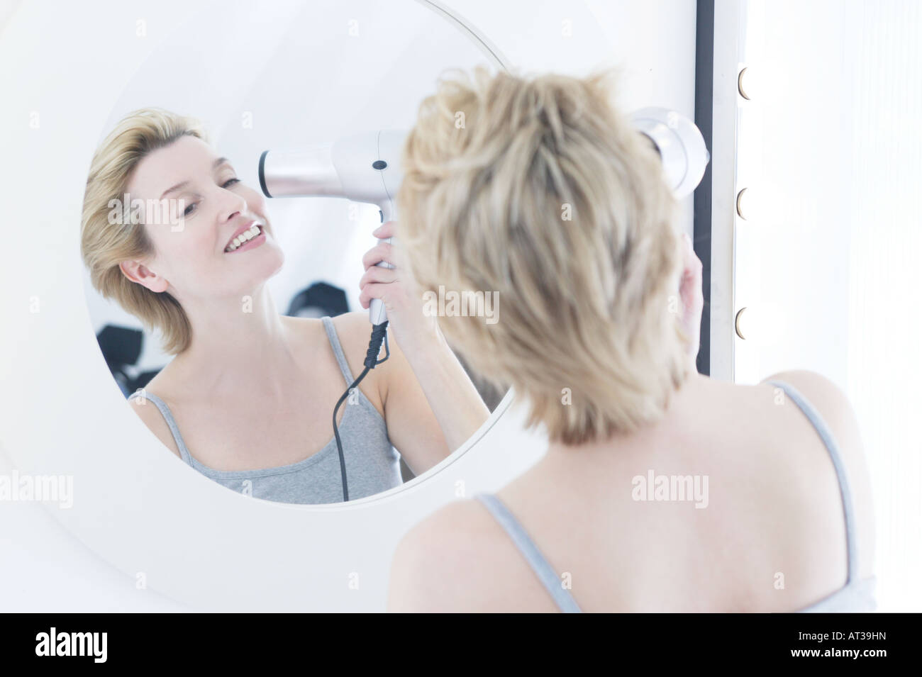 A woman drying her hair with a hairdryer, smiling Stock Photo - Alamy