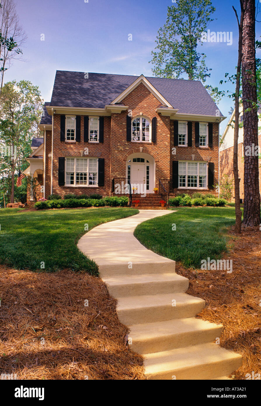 A Concrete Sidewalk Leads Up To A Large Two Story Brown Brick House With Black Shutters Stock Photo - Alamy