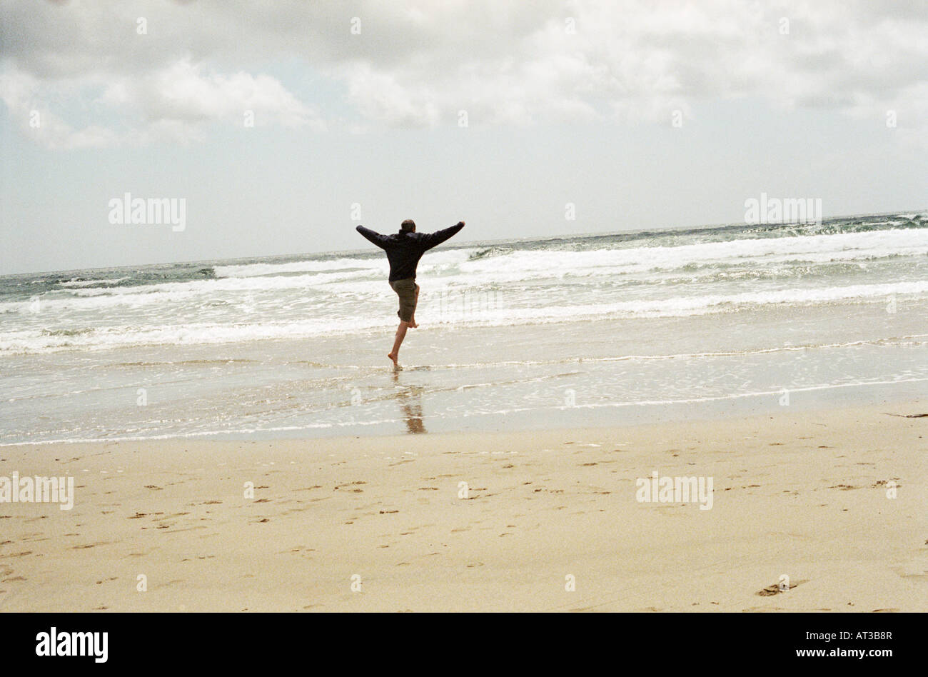 A man skipping through the waves, arms in the air Stock Photo