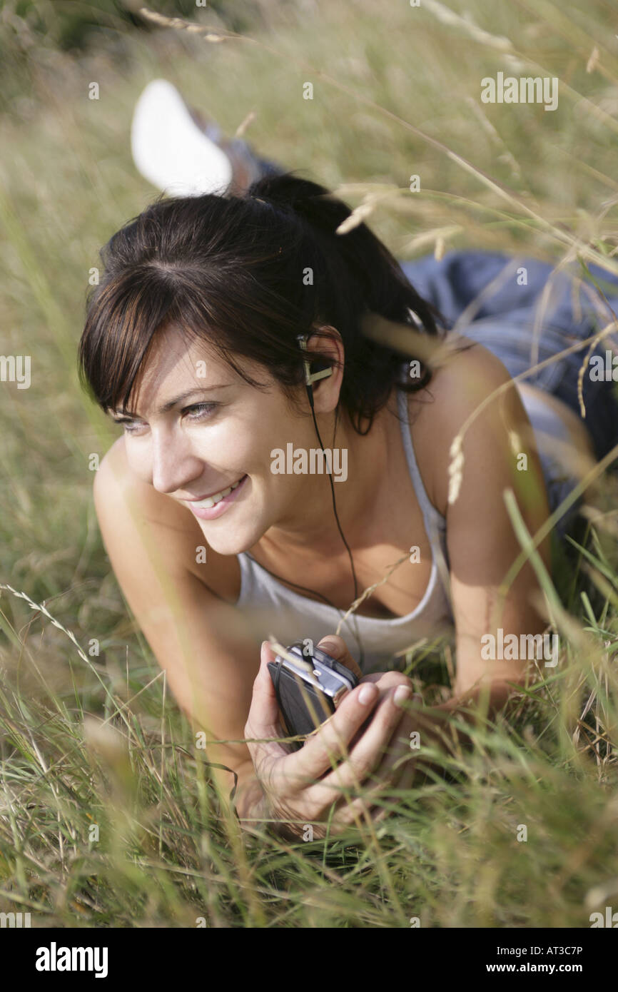 A young woman lying in the grass listening to music, smiling Stock Photo