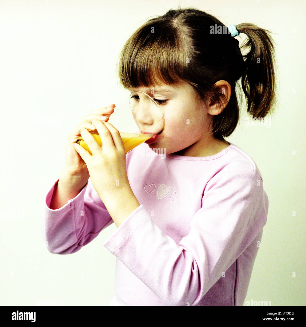 A small girl drinking a glass of orange Stock Photo