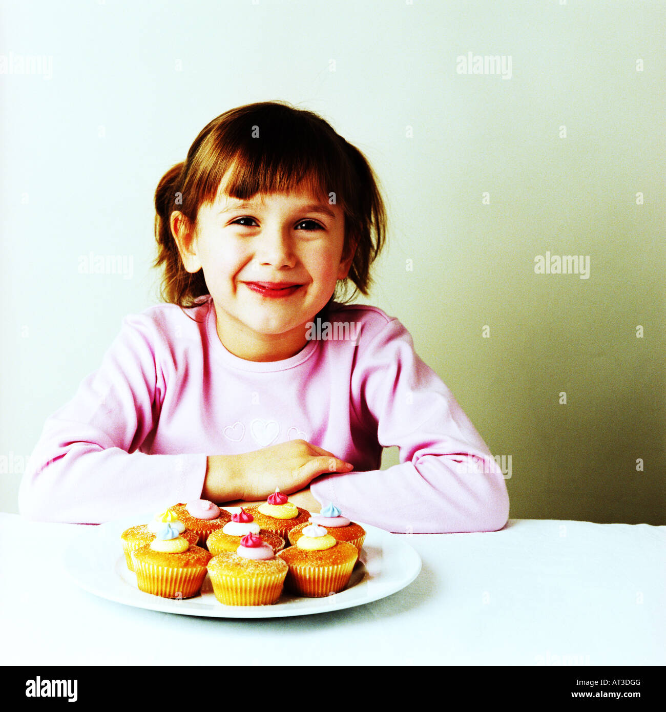 A girl sitting with a plate of fairy cakes Stock Photo