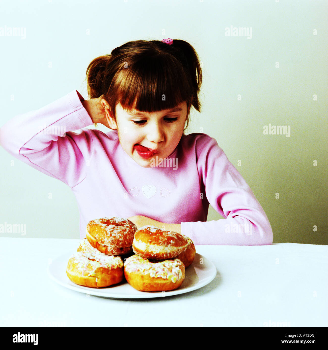 A girl sitting looking at a plate of doughnuts Stock Photo