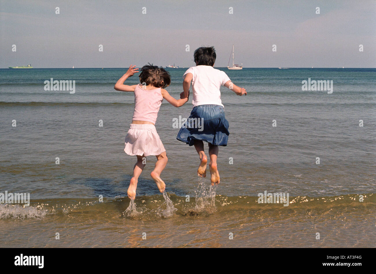 Two young girls jumping in the sea Stock Photo