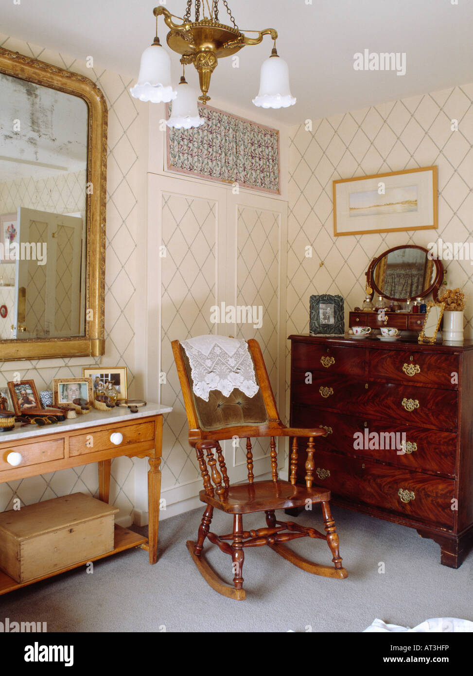 Antique rocking chair and mahogany chest of drawers in country bedroom with trellis wallpaper Stock Photo