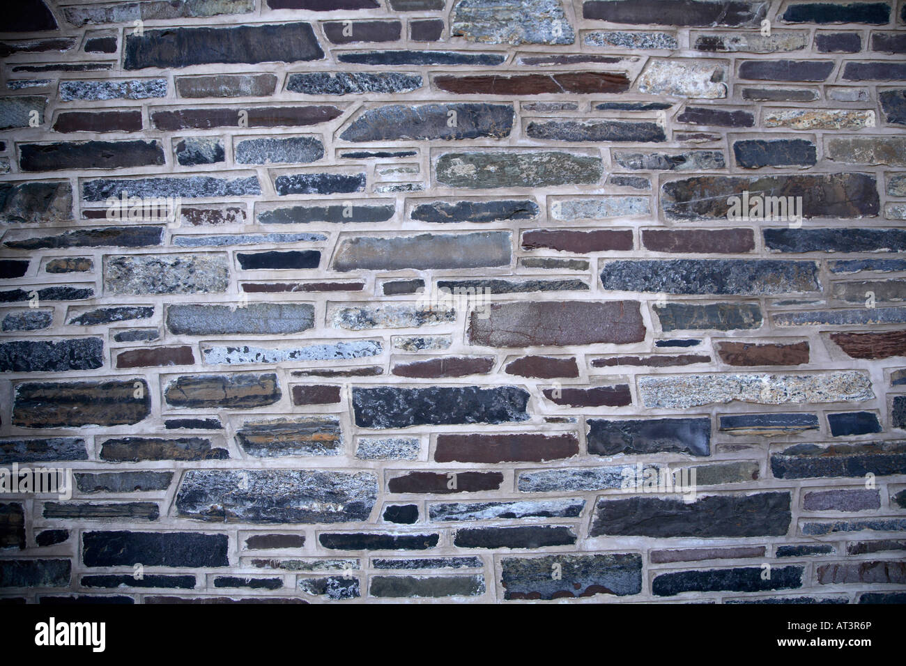 Varied stone wall.  Flat oblong stones in varing widths and materials with thick concrete around them. Stock Photo