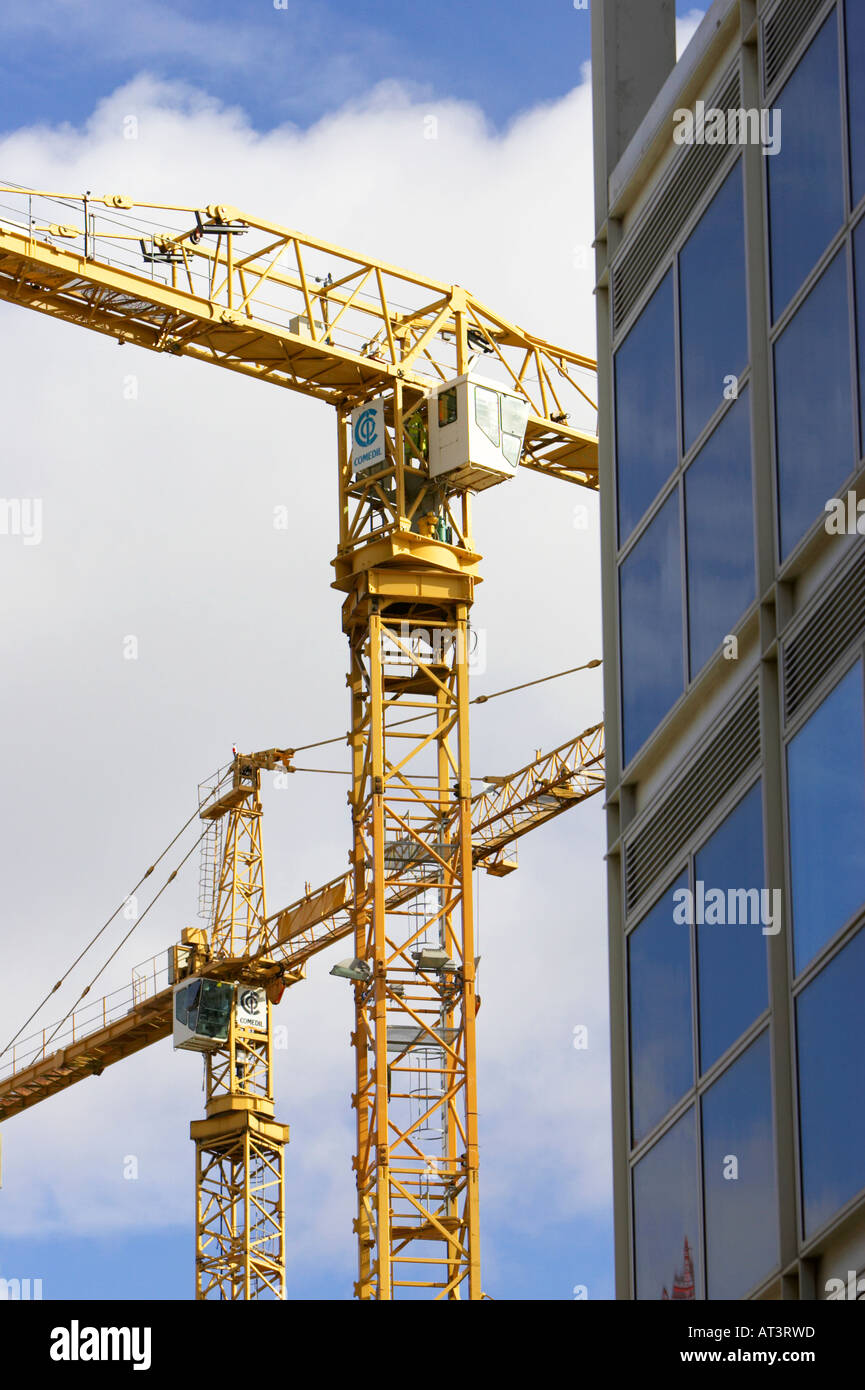 yellow cranes against blue cloudy sky working on construction site near plate glass building in Belfast City Centre Stock Photo