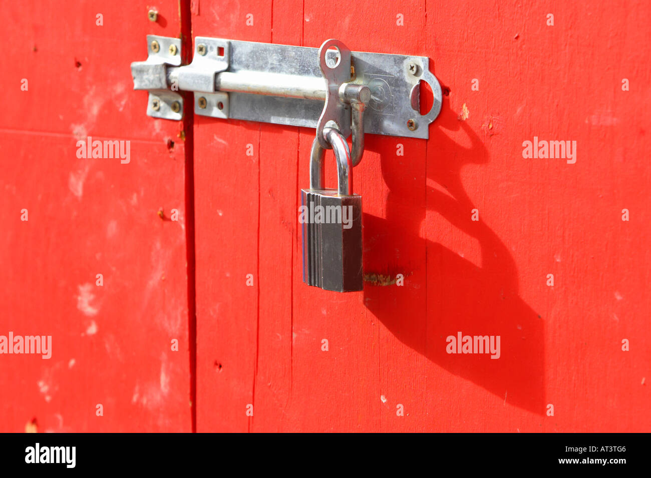 new hasp and staple with padlock attached to secure a red painted wooden door in Belfast City Centre Stock Photo
