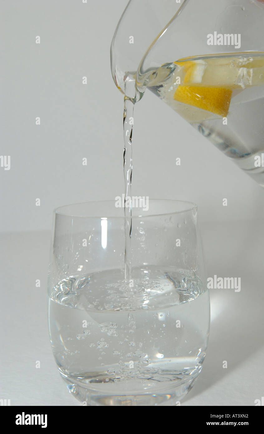 Water pouring from Glass Jug into drinking glass with lemon  Stock Photo