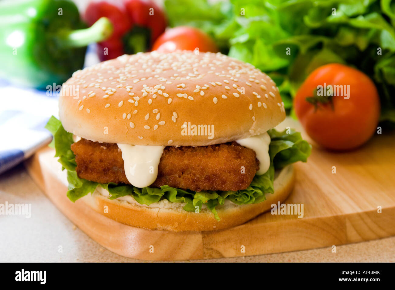 A hot chicken or fish burger & mayonnaise presented with fresh produce on a wooden platter Stock Photo