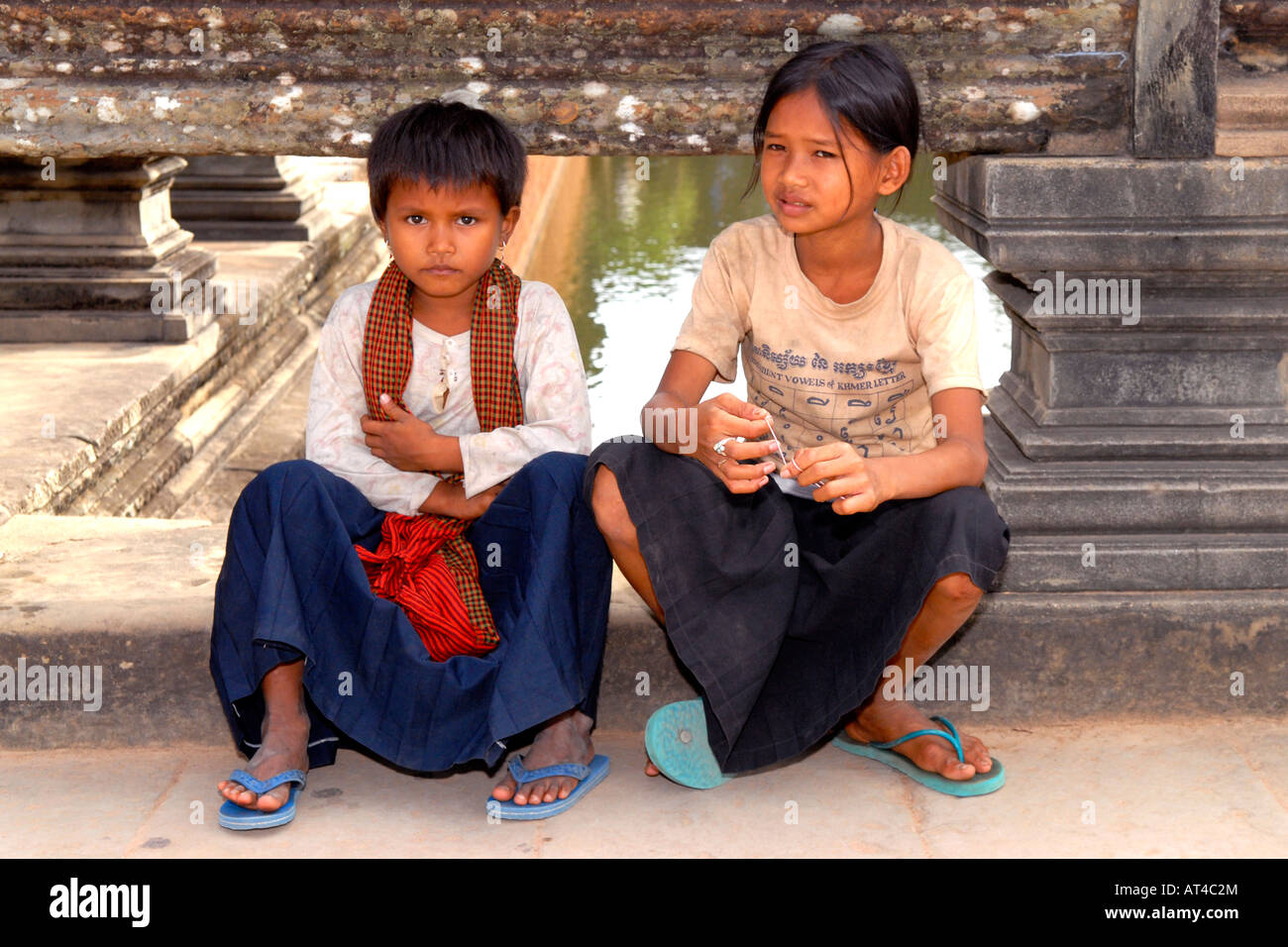 Cambodia , Siem Reap , Angkor Thom Temple , two pretty young local girls rest in the shade on bridge over moat Stock Photo